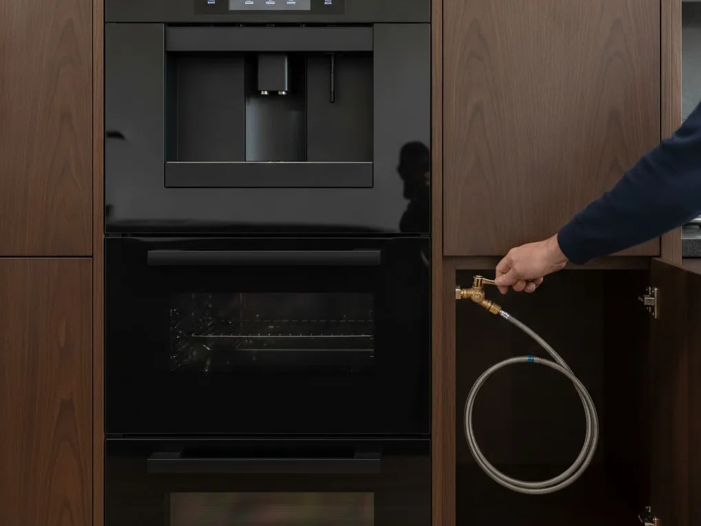 Hand closing a quarter-turn shutoff valve on the water line that feeds a plumbed built-in coffee machine